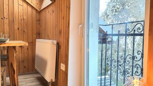 Un interior de madera con una mesa de comedor, un radiador y un ventanal que ofrece vistas a un balcón y árboles.