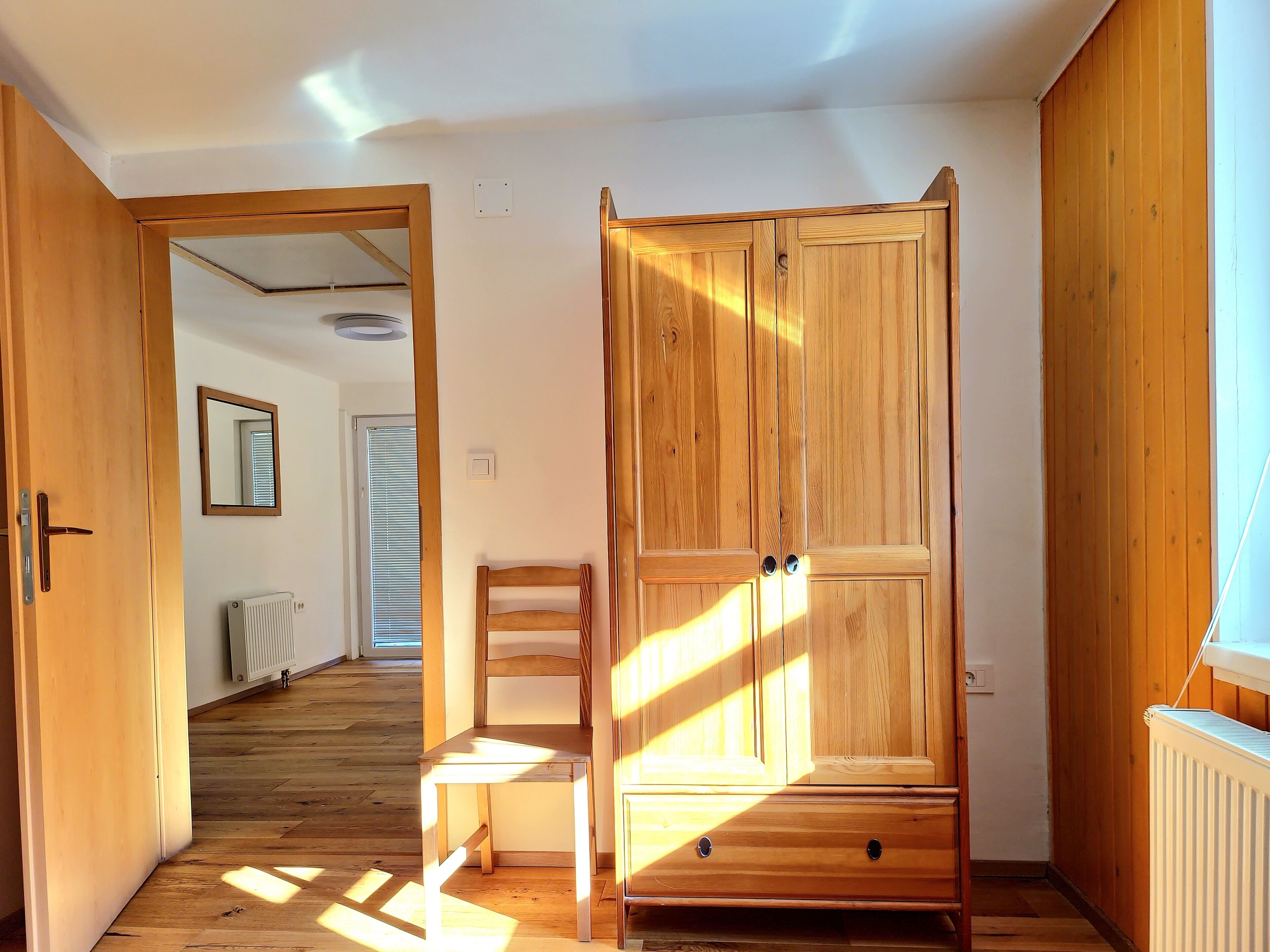 A room with wooden flooring, a wooden wardrobe, a wooden chair, and a radiator.