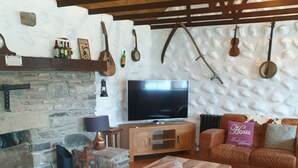 A cozy living room with a stone fireplace, leather sofas, a wooden coffee table, and a television. - Traditional Irish cottage with views of Slieve Patrick (Downpatrick)