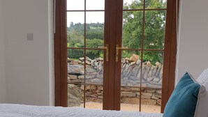 A bedroom with a large window, a bed with white bedding, and a view of a rocky outdoor area. - Traditional Irish cottage with views of Slieve Patrick (Downpatrick)