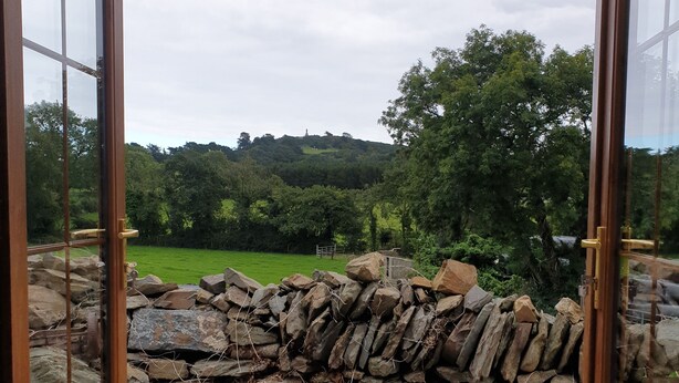 A stone wall with a gravel path leading to a scenic view of a green landscape and trees. - Traditional Irish cottage with views of Slieve Patrick (Downpatrick)