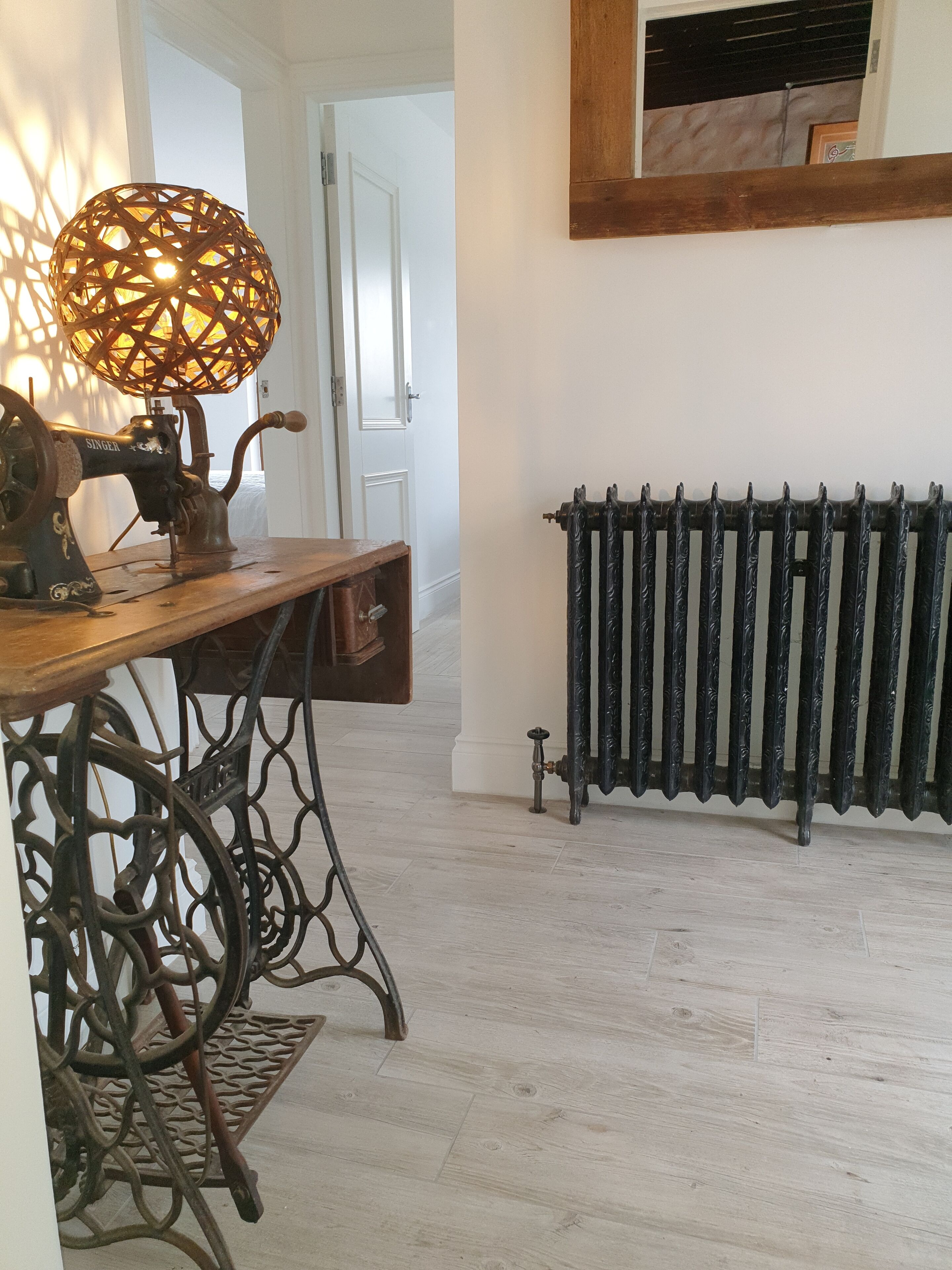 En ældre Singer symaskine står på et træbord, med en radiator og en dør i baggrunden.