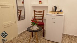 A compact kitchenette with a refrigerator, a small table with a vase of flowers, a chair, and a mirror. - Aida Guest House (Nazareth)