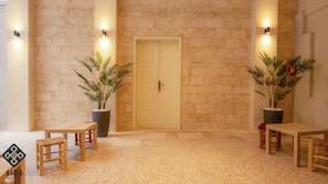 A lobby with a stone wall, a double door, two potted plants, and two wooden tables with chairs. - Aida Guest House (Nazareth)
