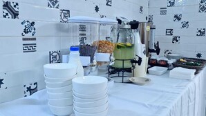 A buffet setup with white plates, bowls, and a beverage dispenser. - Aida Guest House (Nazareth)