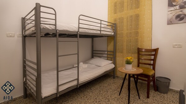 Habitación con literas, una mesita pequeña y una silla, un bote de basura y una cortina estampada.