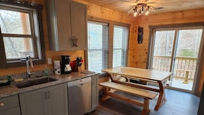 Una cocina con armarios de madera, encimera de granito, un lavamanos, cafetera y una mesa de madera con bancos.