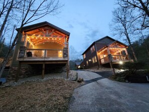 Two wooden cabins with balconies, connected by a pathway, surrounded by trees. - Teddy Bear Cabin-Comfy and Convenient! Close to local attractions. (Sevierville)