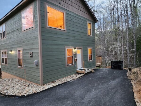 A two-story house with a green exterior, multiple windows, and a paved driveway. - Teddy Bear Cabin-Comfy and Convenient! Close to local attractions. (Sevierville)