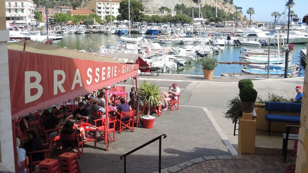A marina with boats docked, a restaurant named 'BRASSERIE GLACIER' with outdoor seating, and a hillside in the background. - Le Pêcheur Revisité by Winkyhouse Cassis (Cassis)