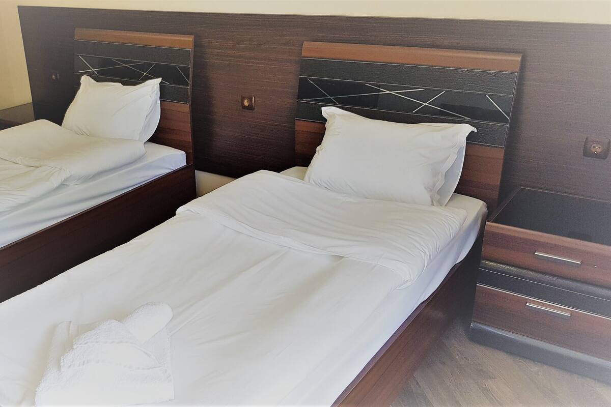 Two single beds with wooden headboards, white linens, and a small bedside table with a lamp.