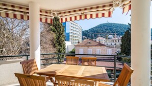 A wooden table and chairs under a striped awning on a balcony with a view of buildings and a hill. - Apartment Villa Claudia (Dubrovnik)