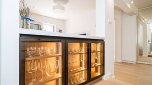 A modern kitchen with a marble countertop, wooden cabinets, and a glass display case filled with wine glasses. - Apartment Villa Claudia (Dubrovnik)