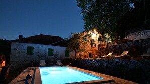 A swimming pool with lounge chairs and a stone wall. - Apartment Rural Podastrana (Sinj)
