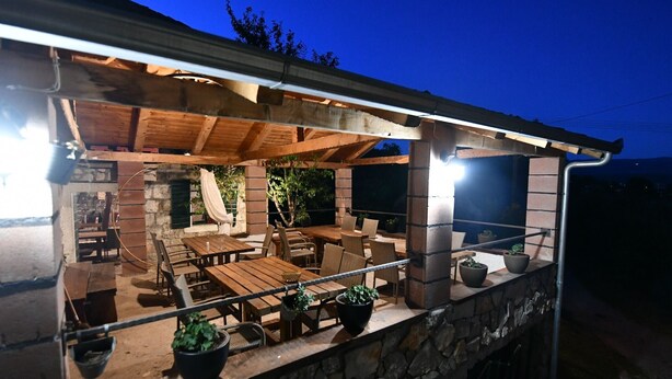 An outdoor patio with wooden furniture and stone walls, featuring a brick fireplace and potted plants. - Apartment Rural Podastrana (Sinj)