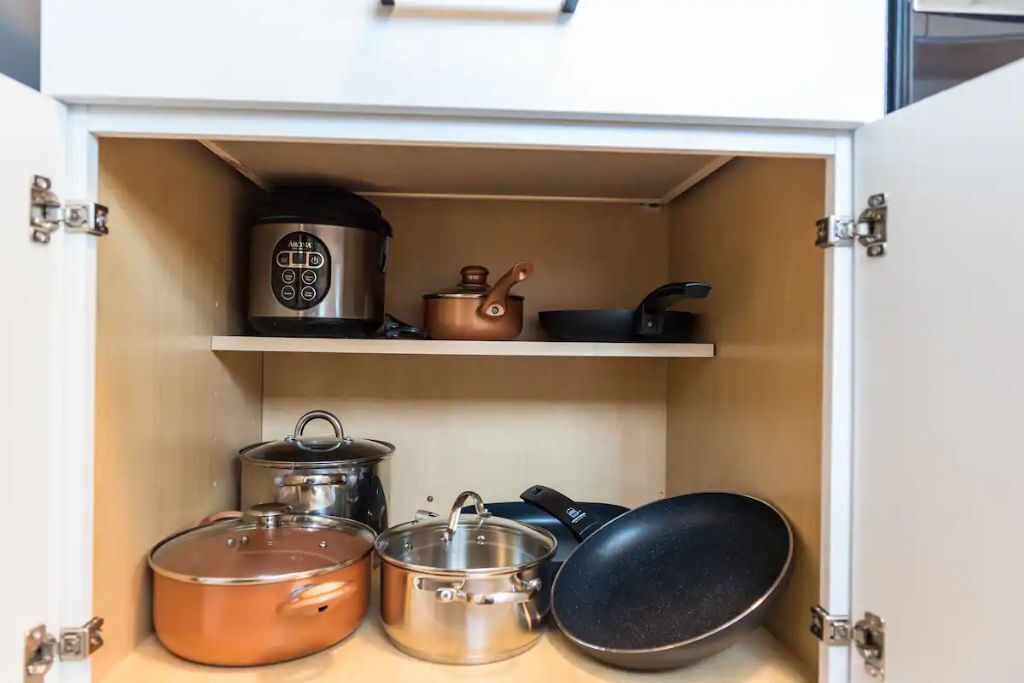 Un armario de cocina con ollas, sartenes y una cocedora de arroz.