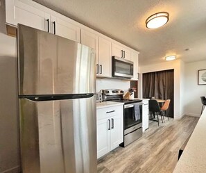 Compact kitchen with modern appliances, stove, and oven, featuring a dining area with a chair and table.