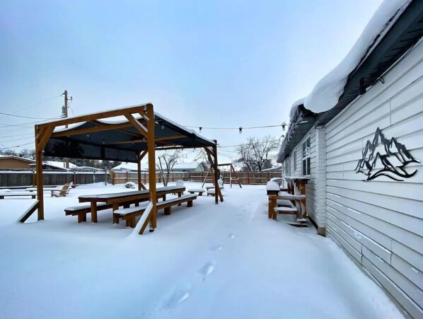 Relax under the pergola's shade, surrounded by snow-covered grounds and a mountain-inspired building.