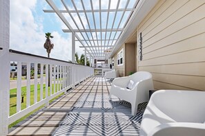 Relax in a comfortable seating area under a shaded pergola with a palm tree in the background.