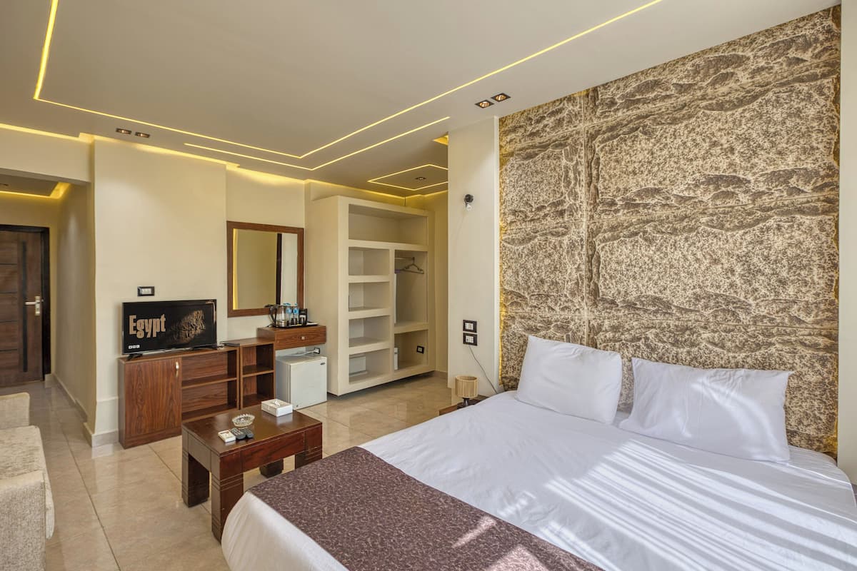 A hotel room with a large bed, a wooden dresser, a television, a wardrobe, and a stone-textured accent wall.
