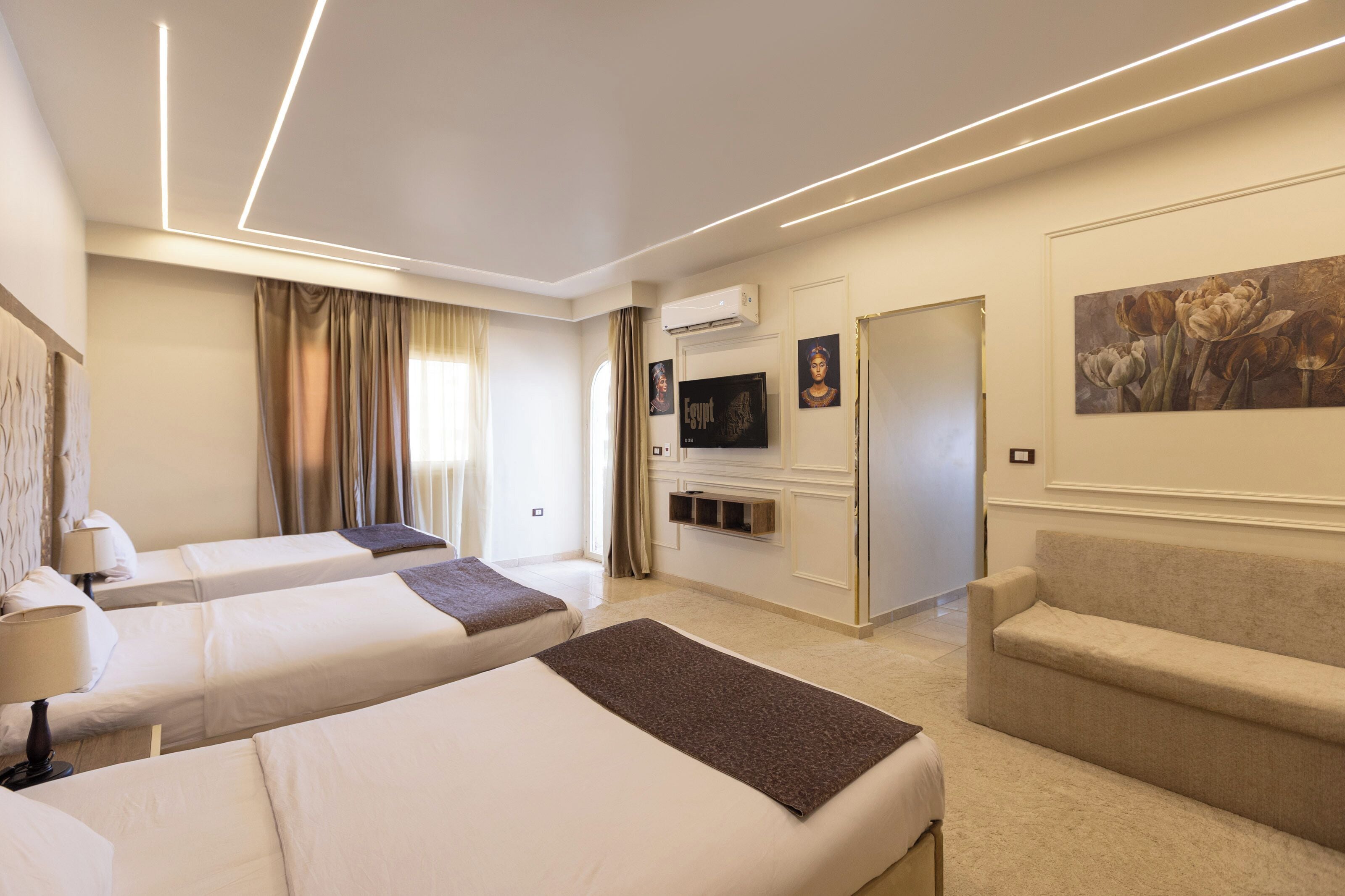 Une chambre d’hôtel avec deux lits, un canapé, une télévision et un tableau au mur.