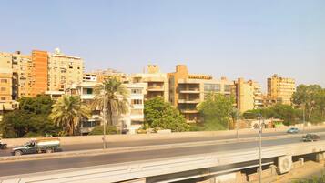 Un edificio de varios pisos con balcones, una palmera y una calle con vehículos.