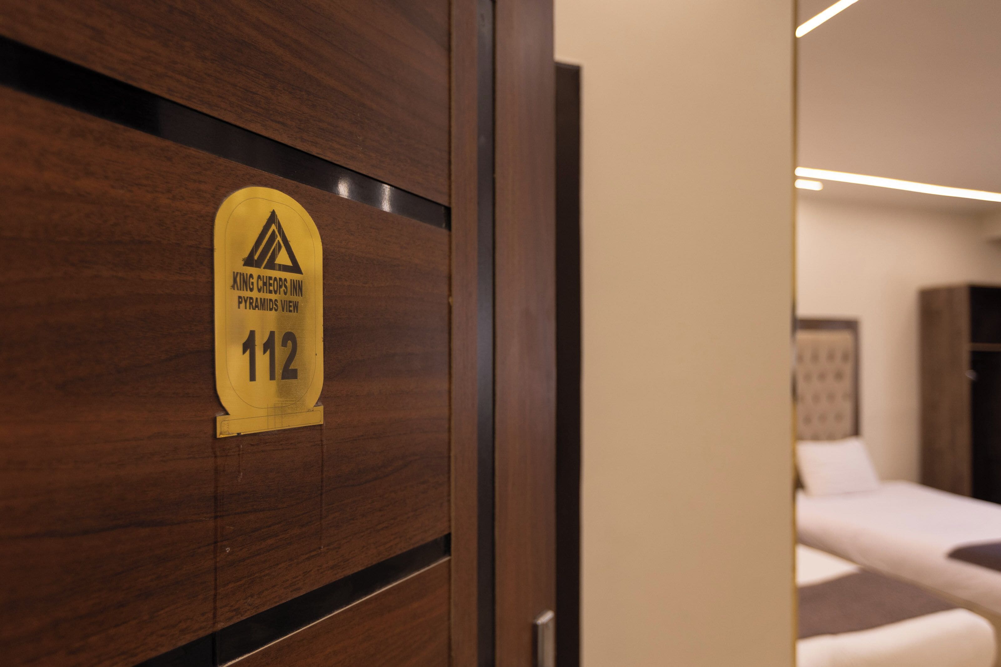 A hotel room door with a sign indicating room number 112, a bed, and a view of the pyramids.