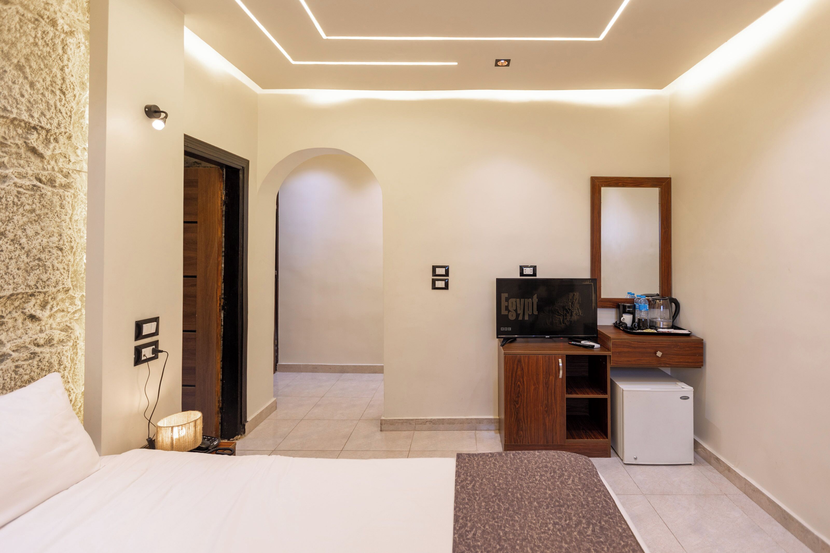 Una habitación de hotel con cama, escritorio con computadora, televisión y un refrigerador pequeño.