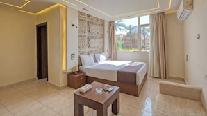 A modern hotel room with a large bed, a small table, a sofa, and a view of palm trees and buildings outside the window. - King Cheops Inn (Giza)
