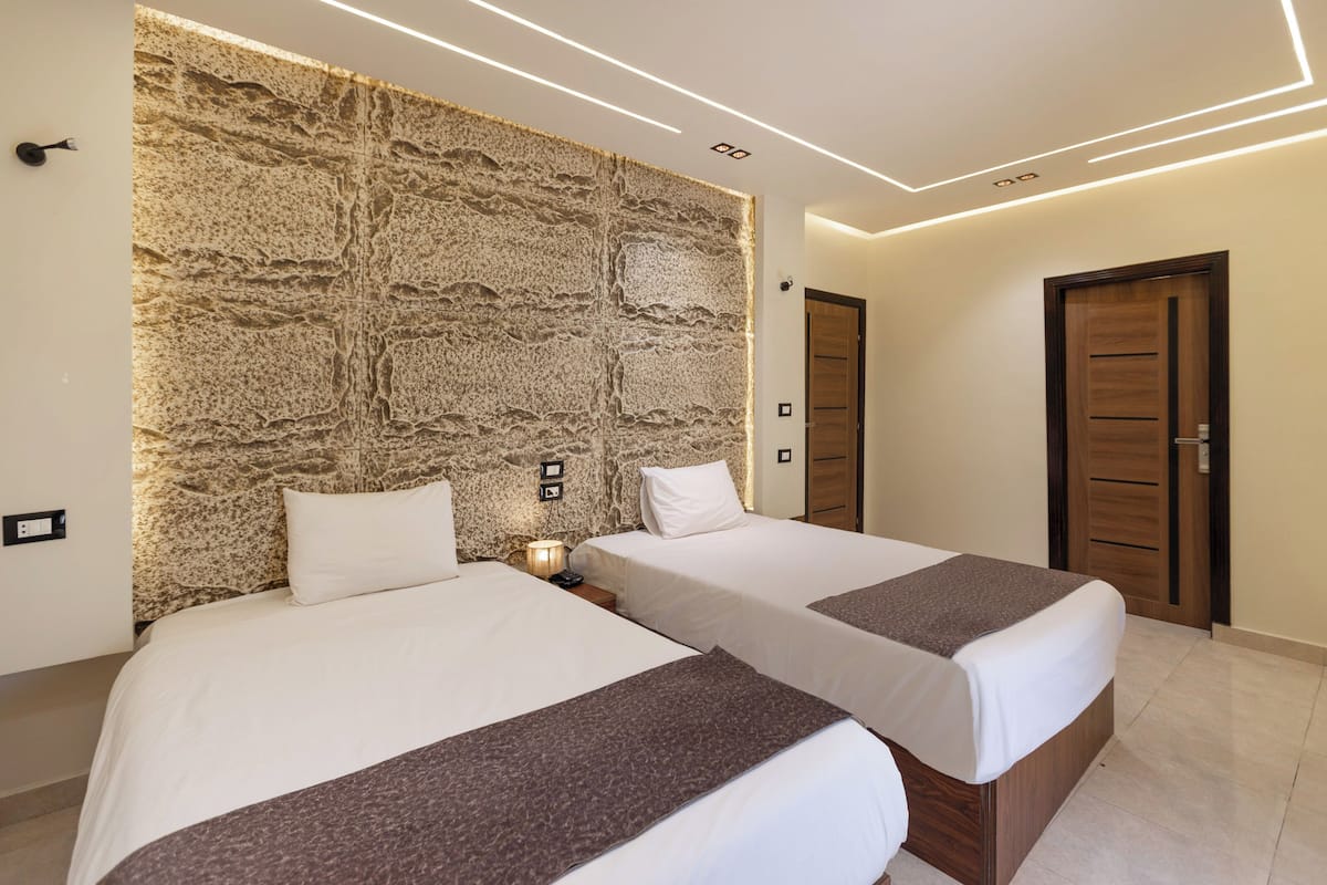 A hotel room with two beds, a stone accent wall, modern lighting, and wooden doors.