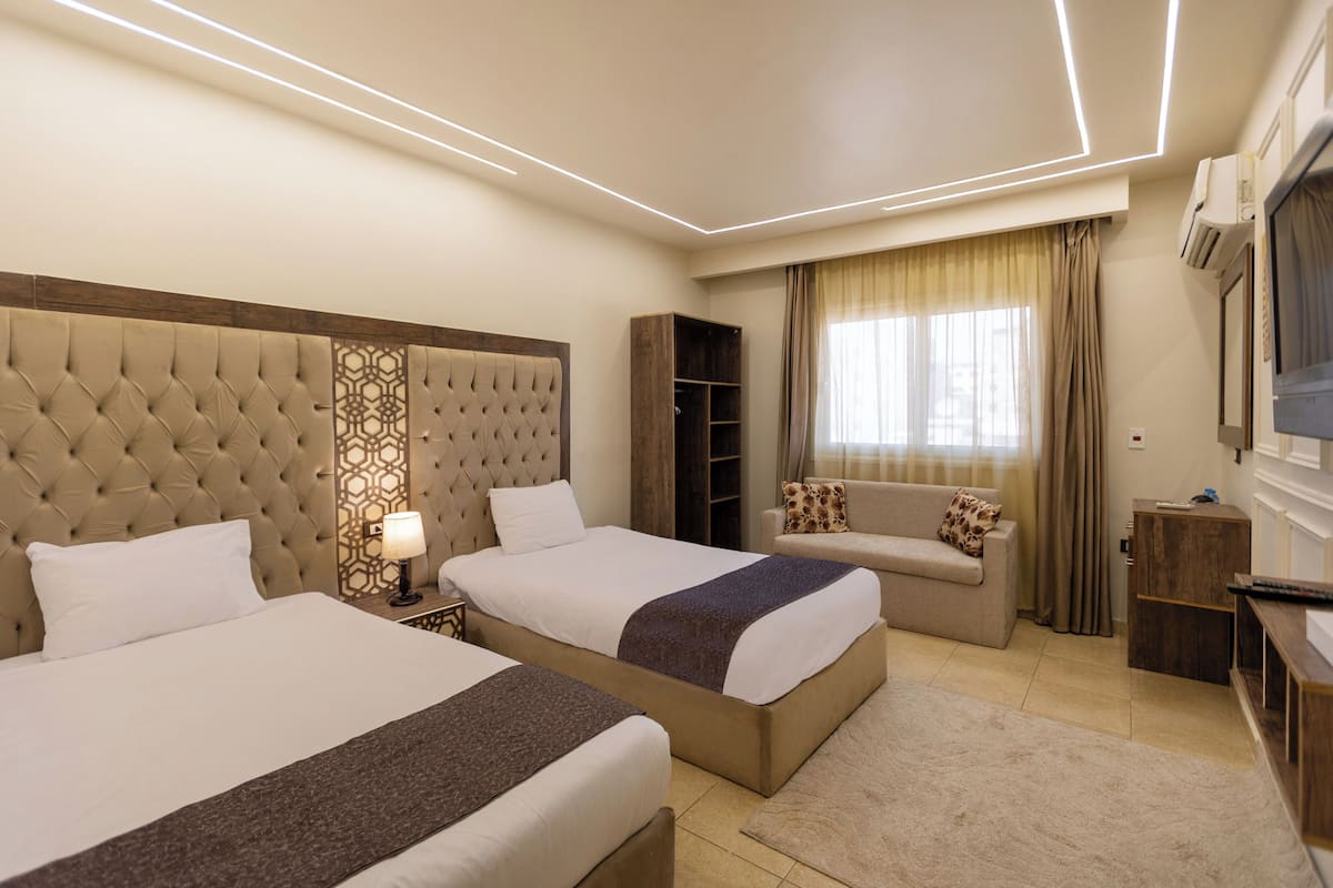 A hotel room with two beds, a sofa, a TV, and a wardrobe.