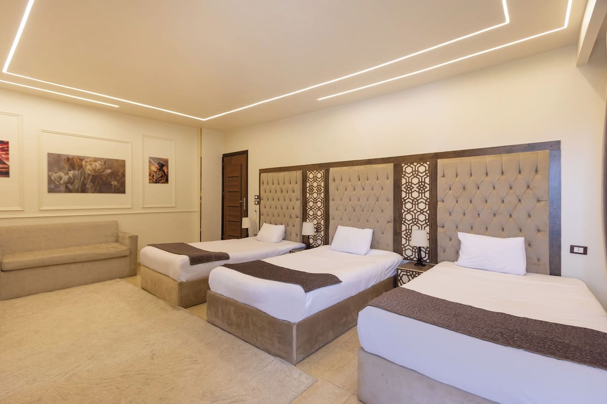 A hotel room with three beds, a sofa, and a decorative wall panel.