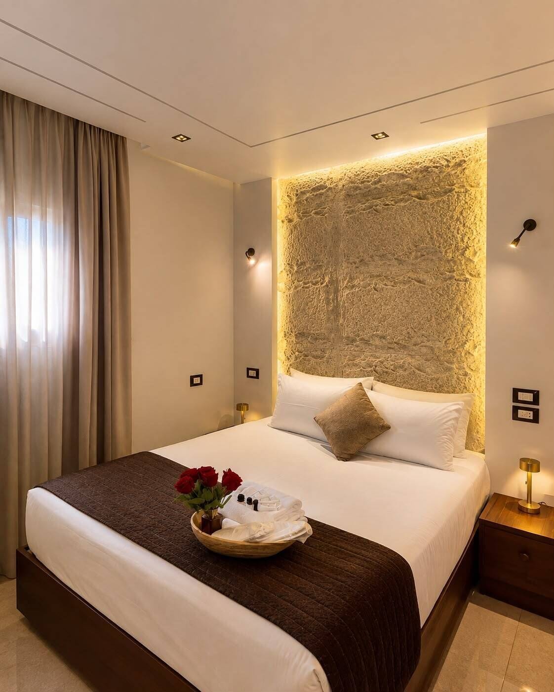 A hotel room with a large bed, a headboard with textured wall design, a bedside table with a lamp, and a window with curtains.