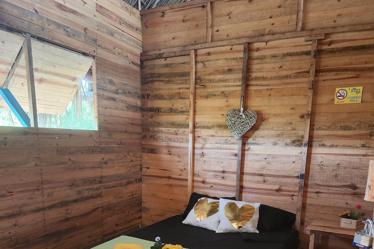 A wooden room with a bed, a small table, and a window.