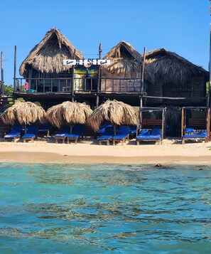 A beachfront property with thatched-roof structures, blue lounge chairs, and a sign reading "Beach Set". - Baru Jet Set Beach & Hostal (Cartagena)