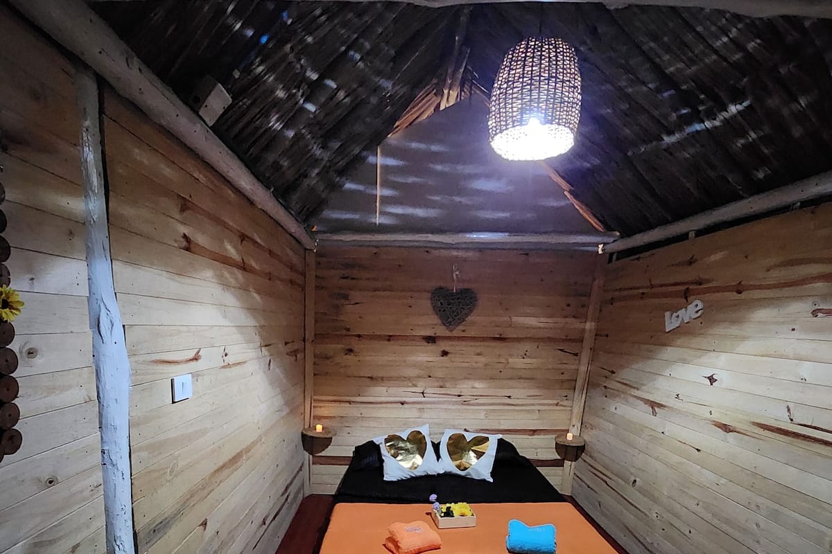 A wooden cabin room with a bed, a heart-shaped decoration, and a hanging light fixture.