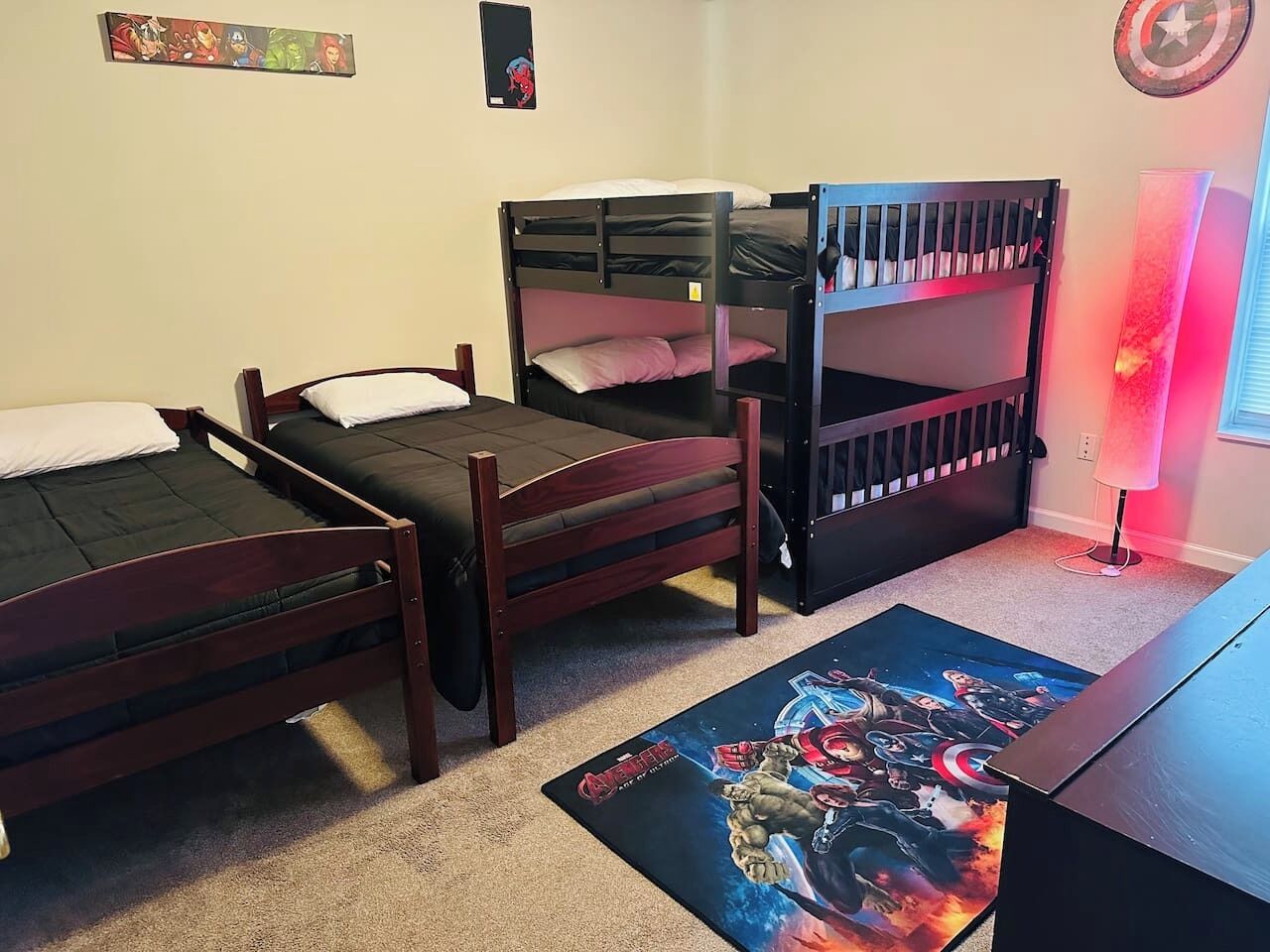 Une chambre avec trois lits superposés, un bureau et une lampe fixée au mur.