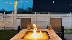 A square outdoor fire pit with a wooden frame and a glass top, surrounded by chairs, under string lights. - The Great Escape, King suite, Kid friendly (Sevierville)
