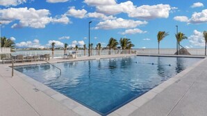 Une piscine rectangulaire à l’eau d’un bleu cristallin, entourée d’une clôture blanche et de palmiers.
