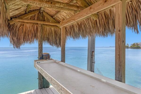Una terraza de madera con techo de paja que da a un mar tranquilo.