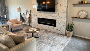 A modern living room with a marble wall, a flat-screen TV, a fireplace, a coffee table, and a sofa.