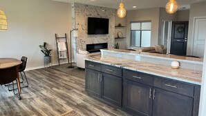 A modern kitchen with dark cabinets, a marble countertop, and pendant lighting.