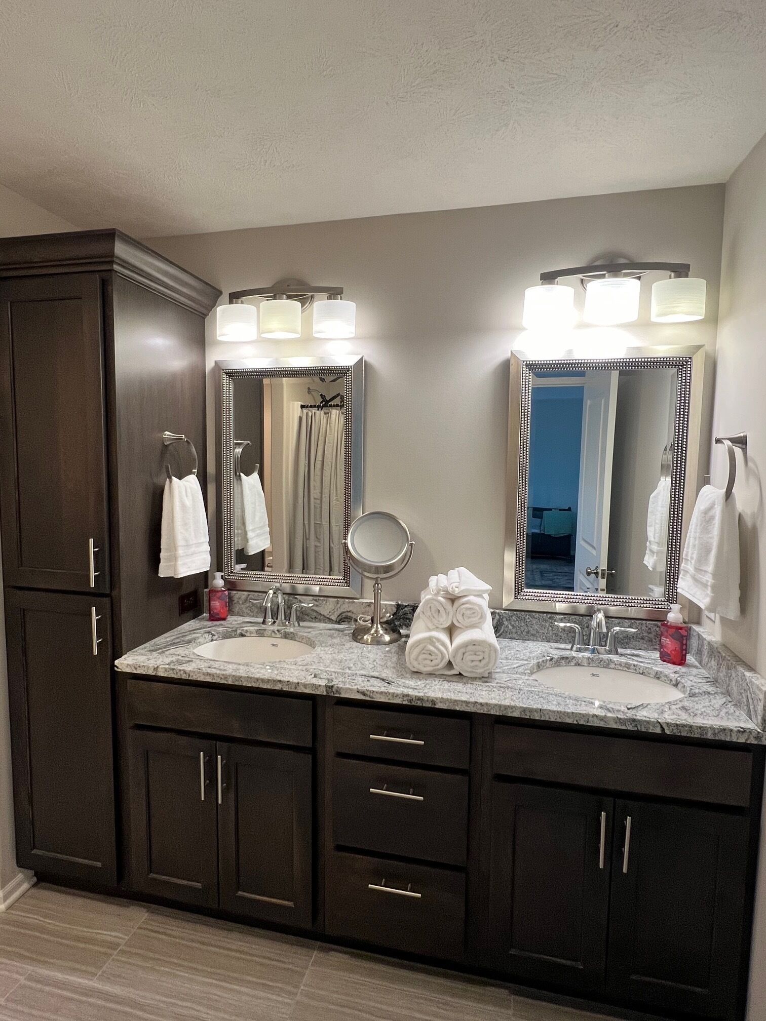Une salle de bain avec des meubles en bois foncé, un lavabo en marbre et deux grands miroirs dotés de lumières à DEL.