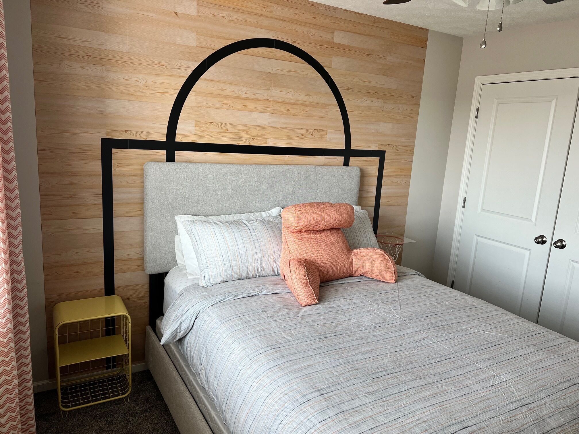 A bed with a grey headboard, a small yellow side table, and a white door in the background.