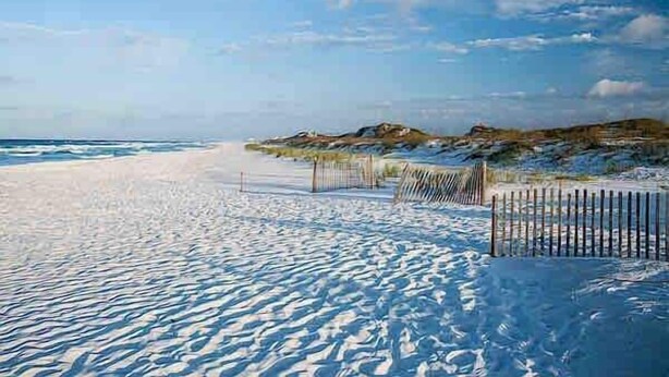Una playa nevada con una valla y terreno rocoso al fondo.