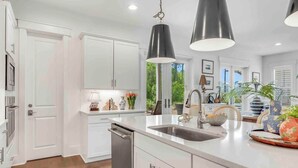 Una cocina moderna con armarios blancos, un lavamanos de acero inoxidable e iluminación colgante.