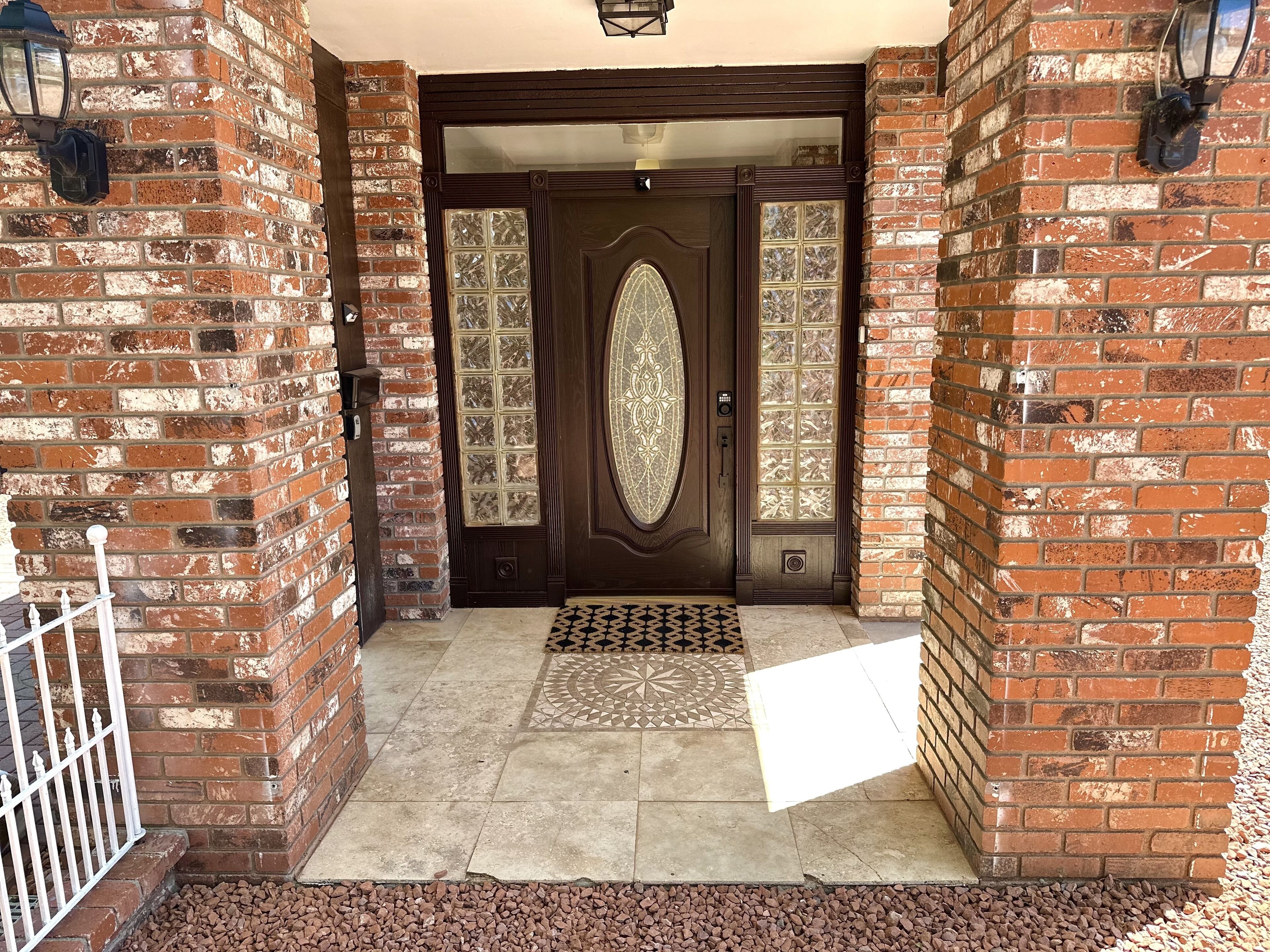 A brick entrance with a decorative glass door and a metal gate.