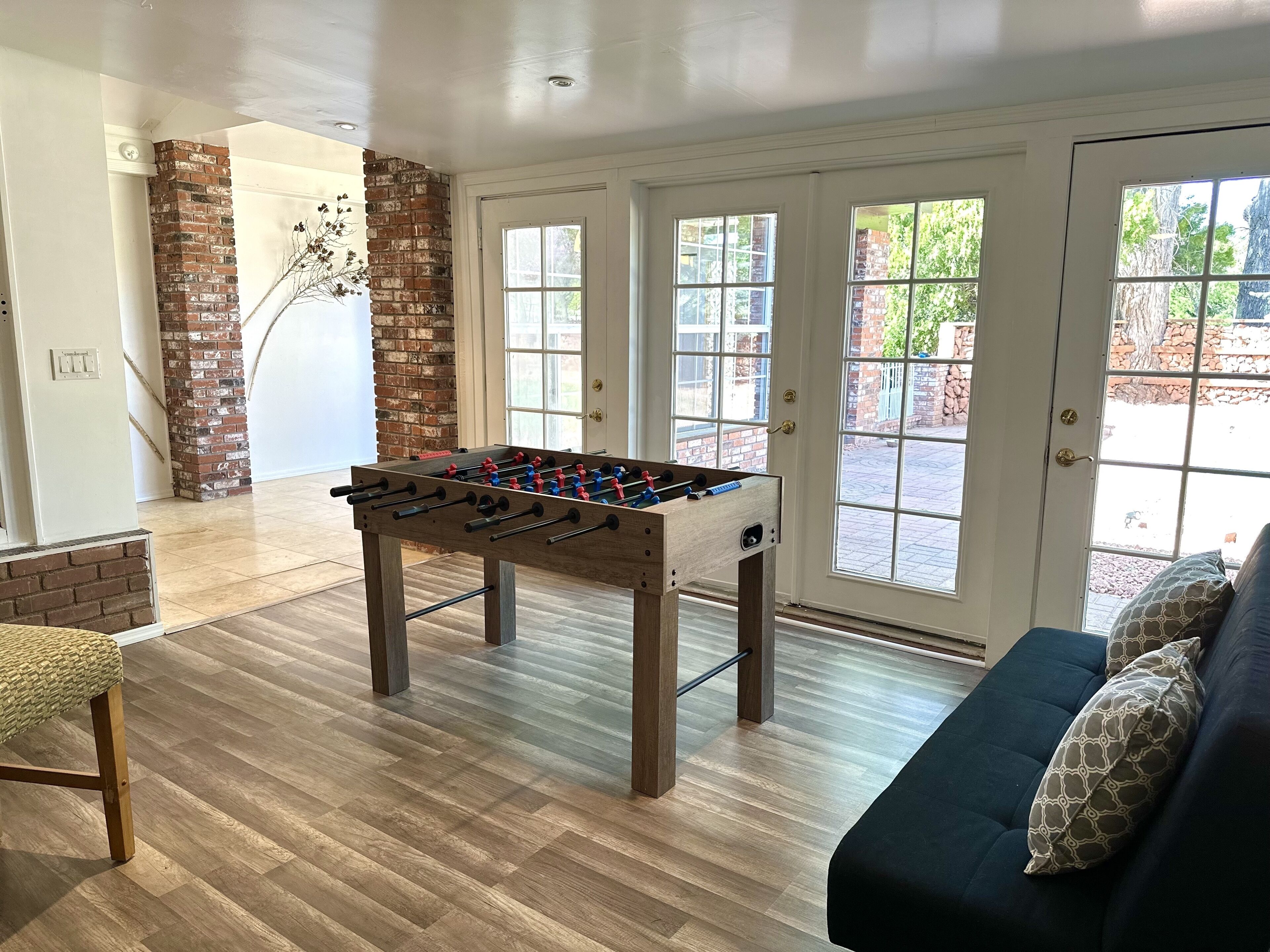 A room with a foosball table, a brick wall, and a large window.