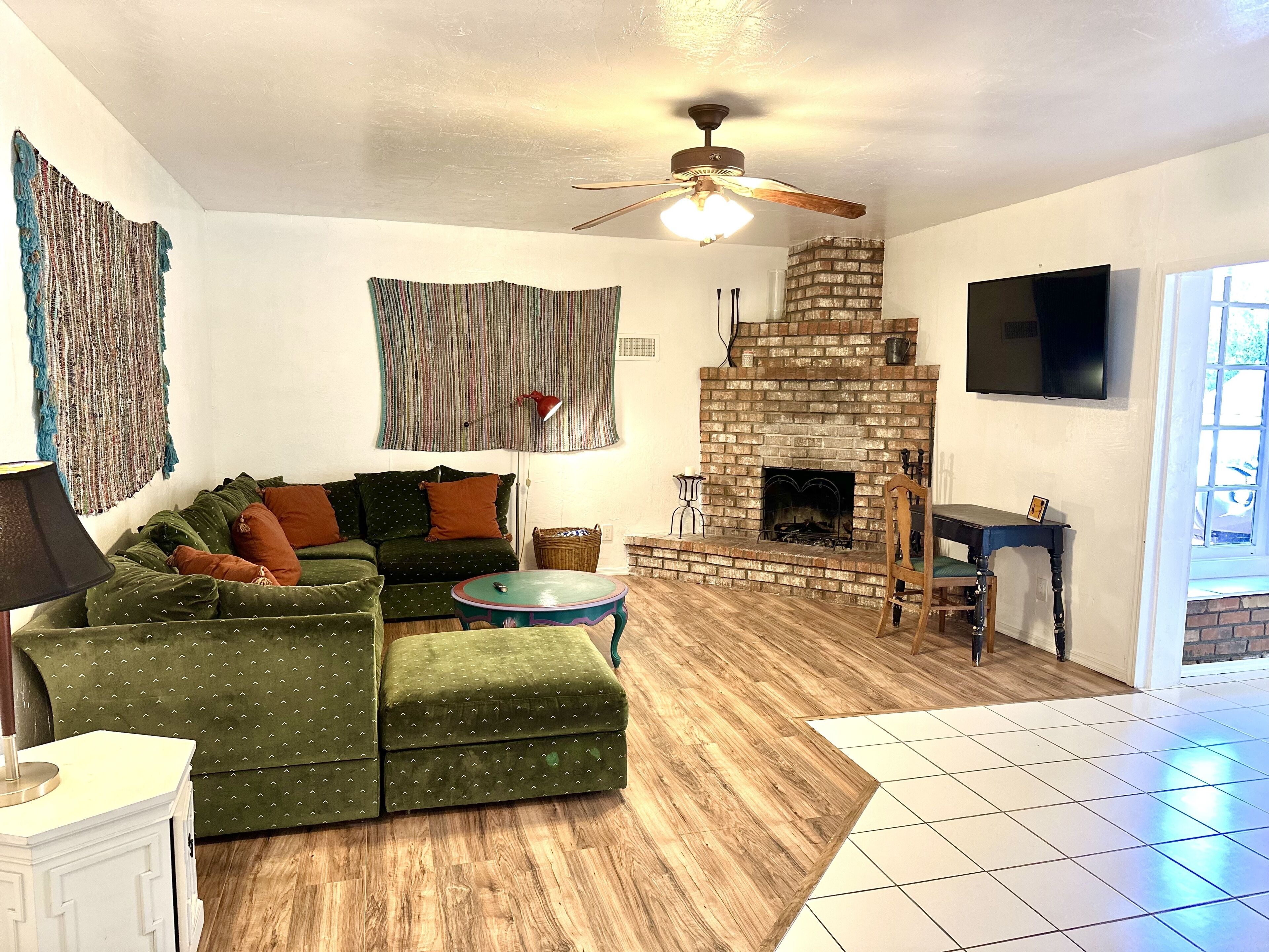 A living room with a green sofa, a small table, a fireplace, and a ceiling fan.
