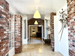 Een hal met openliggende bakstenen muren, een hanglamp, een stoel en een decoratieve plant.